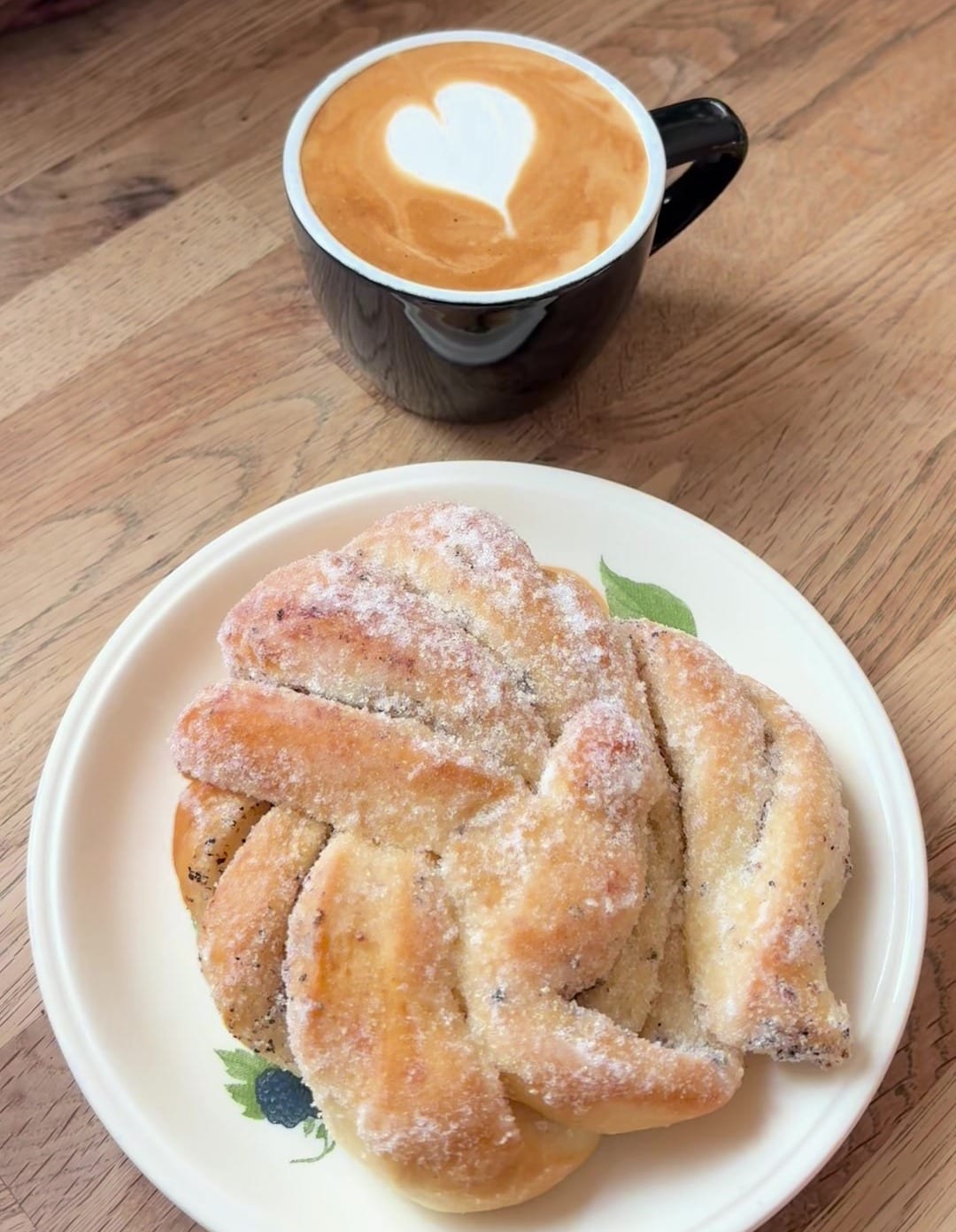 En cappuccino med ett hjärta i mjölkskummet och en sockrad knut på ett fat
